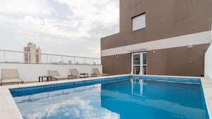 Ein Pool auf dem Dach mit Liegestühlen, einem strahlend blauen Himmel und einem modernen Gebäude im Hintergrund.