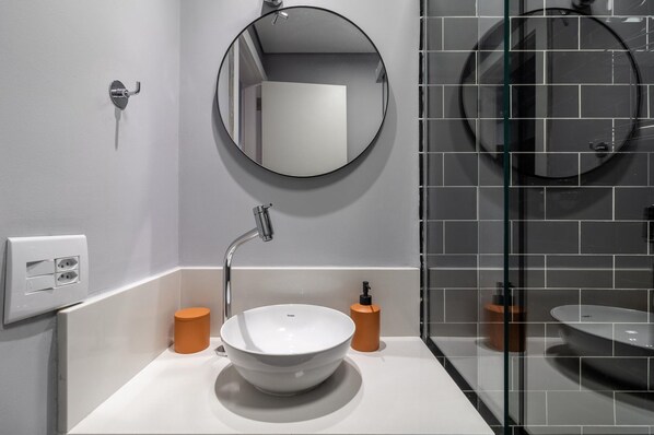A modern bathroom with a white sink, a round mirror, and a glass shower enclosure.