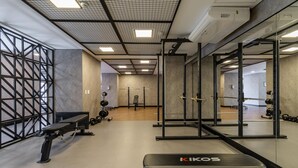Een sportschool met gewichthefapparatuur, een bank en een spiegelwand.
