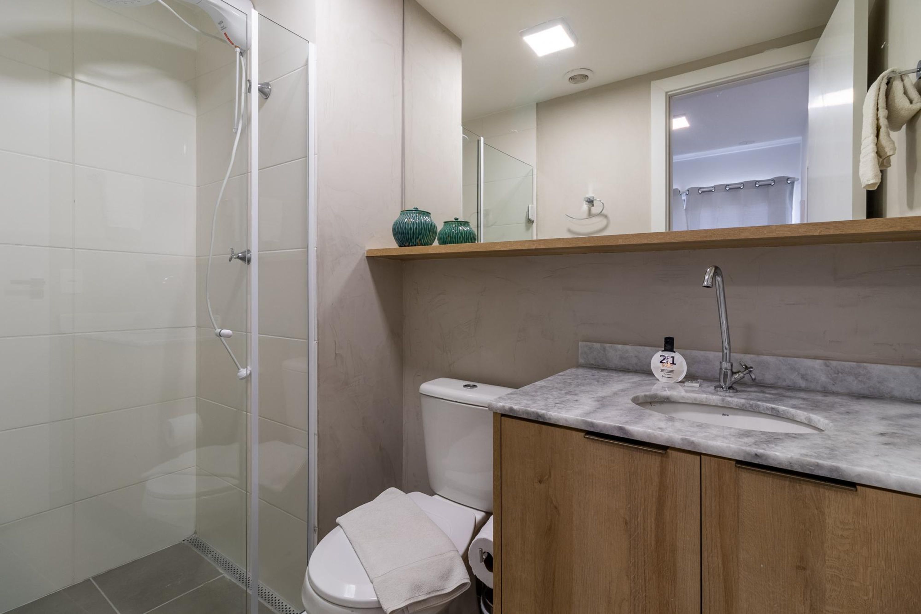 A bathroom with a glass shower enclosure, a toilet, a sink with a marble countertop, and a mirror above the sink.