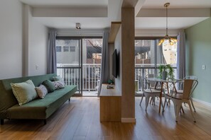 A modern living room with a green sofa, wooden coffee table, and white chairs. A TV is mounted on the wall, and there is a balcony with a view of buildings. - Sa1342-512 in S o Paulo (São Paulo)