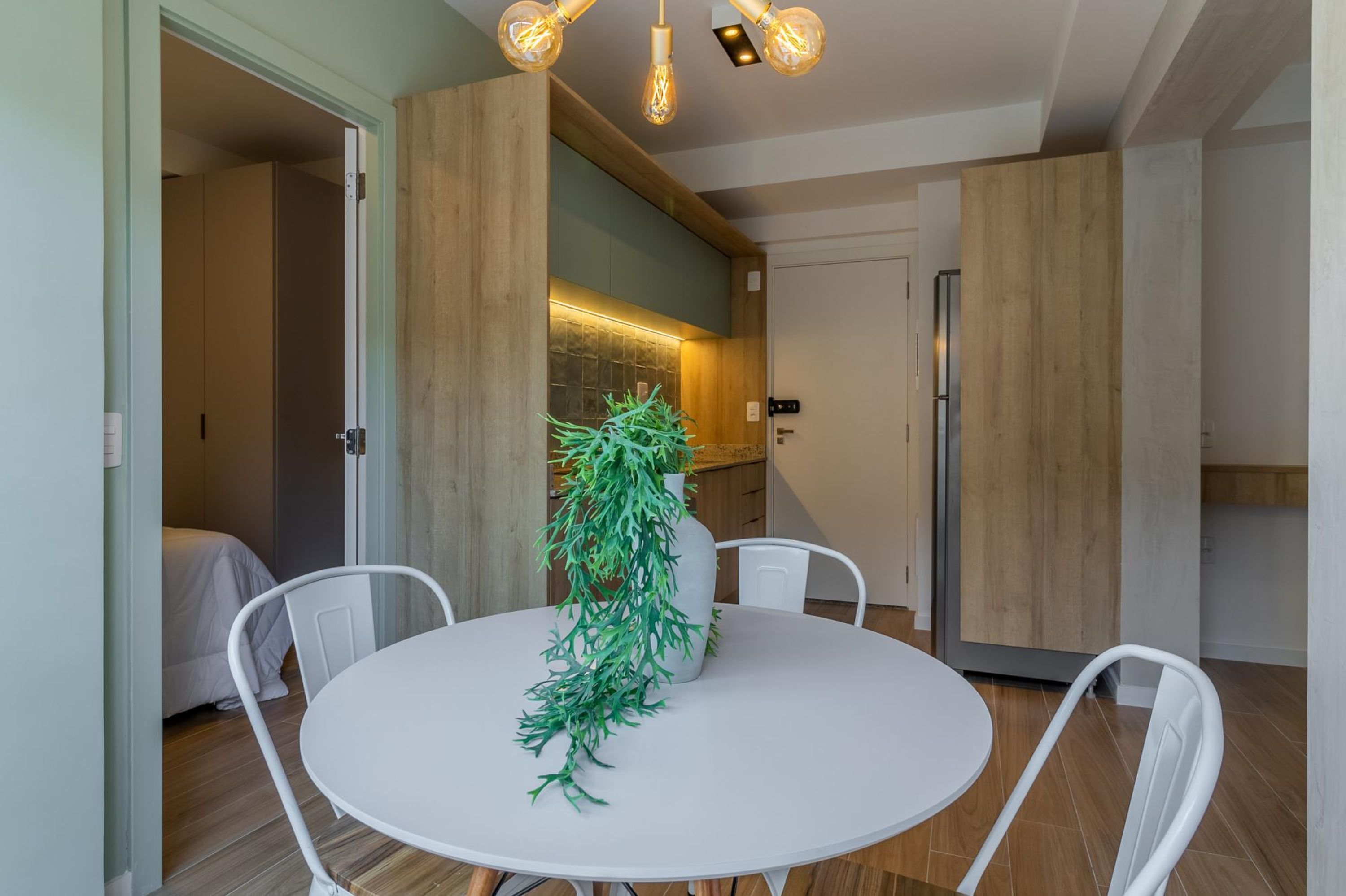 Una cocina moderna con armarios de madera, un comedor con mesa y sillas blancas, y una planta colgante.