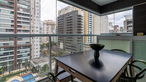 A balcony with a table and chairs, overlooking a cityscape with high-rise buildings and a swimming pool. - Vi0707 in S o Paulo (São Paulo)
