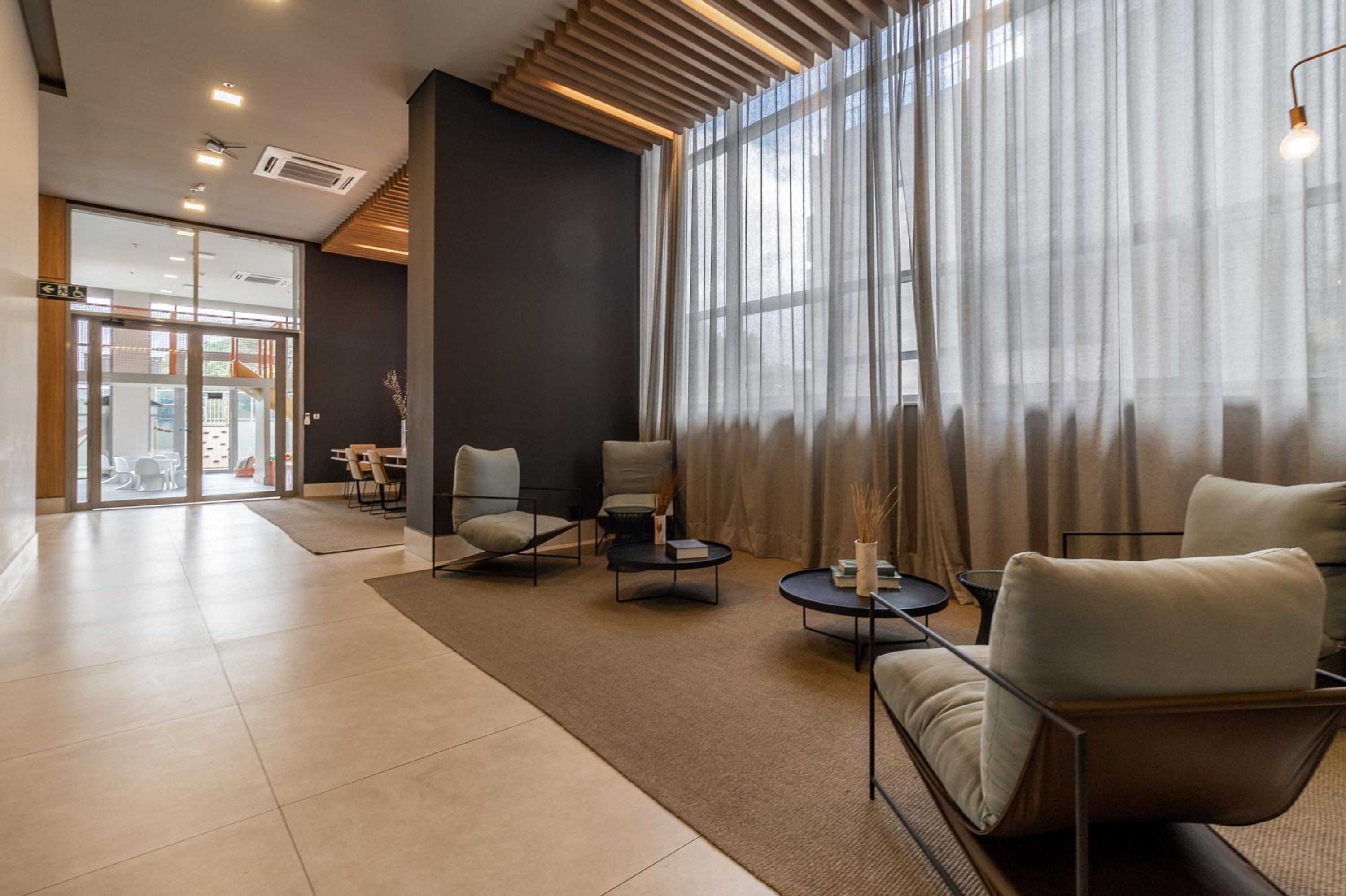 A modern hotel lobby with a seating area, a reception desk, and a view of the outside.