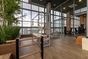 Une salle de sport équipée de matériel d’exercice, dotée de grandes fenêtres et offrant une vue sur la ville.