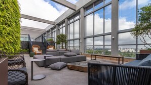 A modern rooftop lounge with a large sofa, round tables, and a staircase leading to an upper level. - HW Rebou As2636-210 (São Paulo)