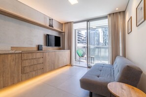 Un espace de vie moderne comprenant un canapé, un téléviseur à écran plat et un balcon offrant une vue sur le paysage urbain.