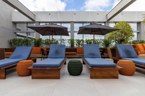 Un espace de détente aménagé sur le toit, avec des chaises longues, des parasols et des plantes en pot.