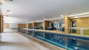 Ein moderner, überdachter Pool mit klarem, blauem Wasser, gefliesten Wänden und blauen Sitzgelegenheiten am Beckenrand.