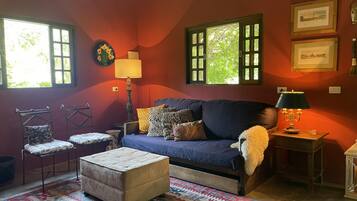 Uma sala de estar aconchegante com sofá, banquinho e poltronas, um tapete estampado e uma luminária.