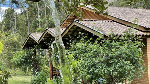 A rustic building with a sloped roof, surrounded by lush greenery and a small garden area with a bench and a table. - Casagon Alves in Gon Alves (Gonçalves)