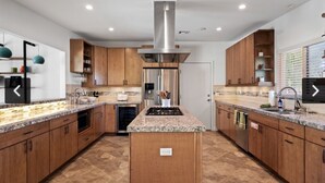 Una cocina moderna con encimeras de granito, electrodomésticos de acero inoxidable, armarios de madera y una isla central.