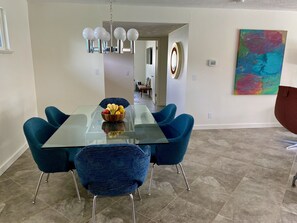 Un espace repas moderne avec une table à plateau en verre, des chaises à revêtement bleu et un centre de table composé d’un saladier à fruits.