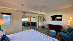 Habitación de hotel con una cama grande, ventilador de techo, televisor, escritorio y un área de descanso con sillas y sofá.