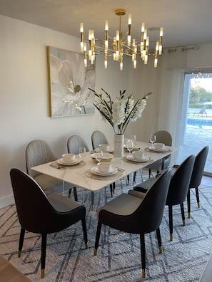 Un comedor con una mesa de mármol, sillas negras, una araña y un cuadro grande con motivos florales en la pared.