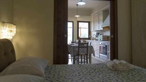 Un dormitorio con una cama, una lámpara de noche y vistas hacia una zona de cocina con una mesa y sillas.