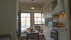 Una cocina con armarios blancos, una mesa de comedor con mantel de lunares y vistas al exterior a través de amplios ventanales.