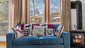 Un sofá azul con cojines estampados, una ventana con cortinas y un estufa de leña.