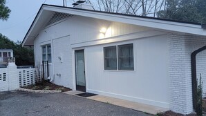 A single-story house with a white exterior, a front door, and a small porch area. - Renovated Suite with 1 queen bed and a Twin. Kitchen & bath for your privacy. (Goldsboro)