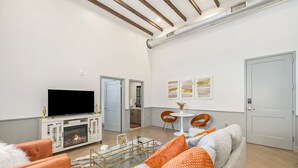 A modern living room with a flat-screen TV, a fireplace, orange and grey furniture, and a dining area with a small table and chairs. - Iconic Morris Ave condo retreat sleeps 6 +rooftop (Birmingham)