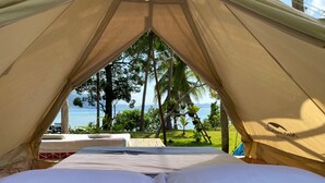 Una tienda de campaña con una cama en su interior, con vistas a un paisaje tropical con palmeras y vista al mar.