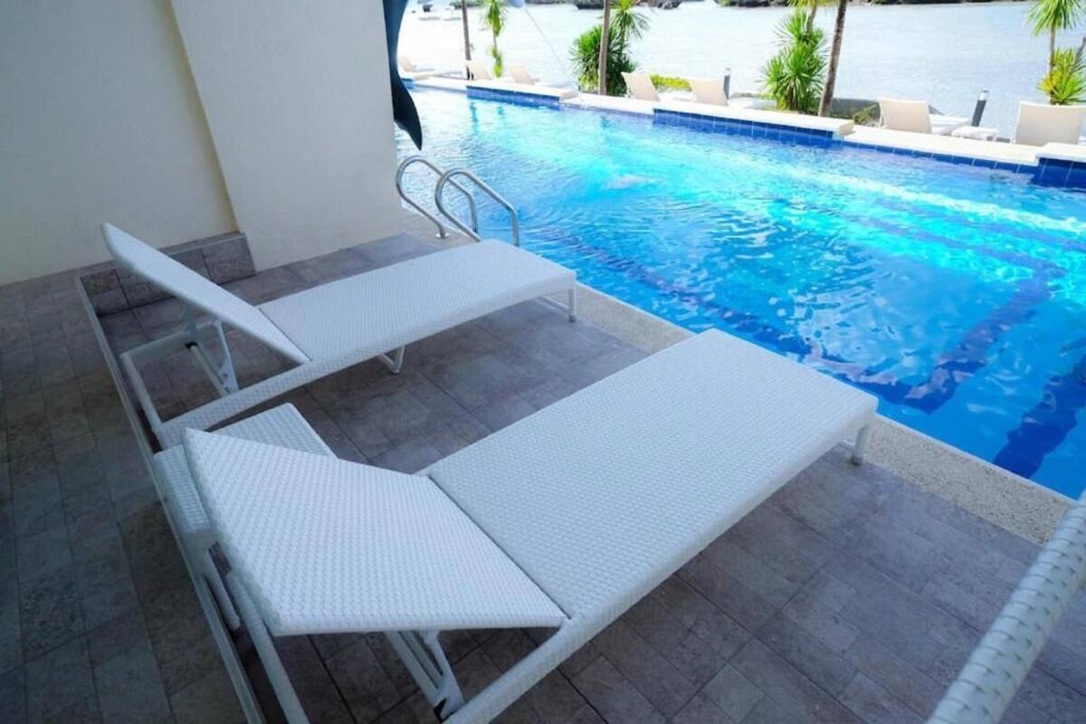 A poolside area with two white lounge chairs and a pool.