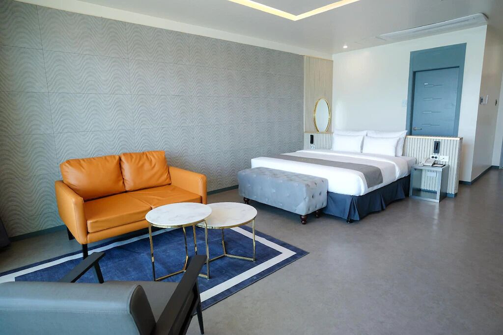 A modern hotel room with a sofa, two round tables, a bed, and a nightstand.