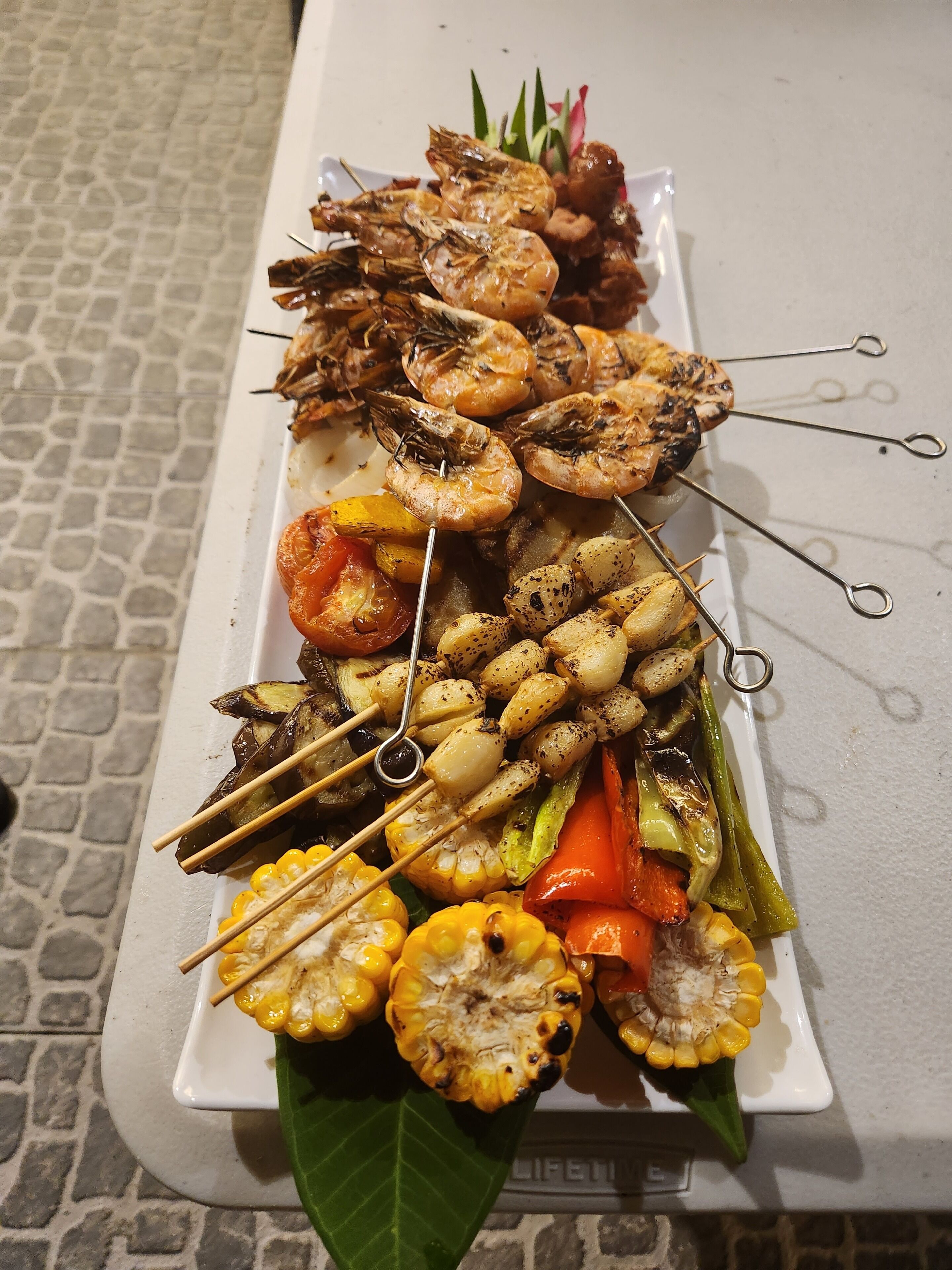 Ett fat med ett urval grillade grönsaker och grillspett med räkor.