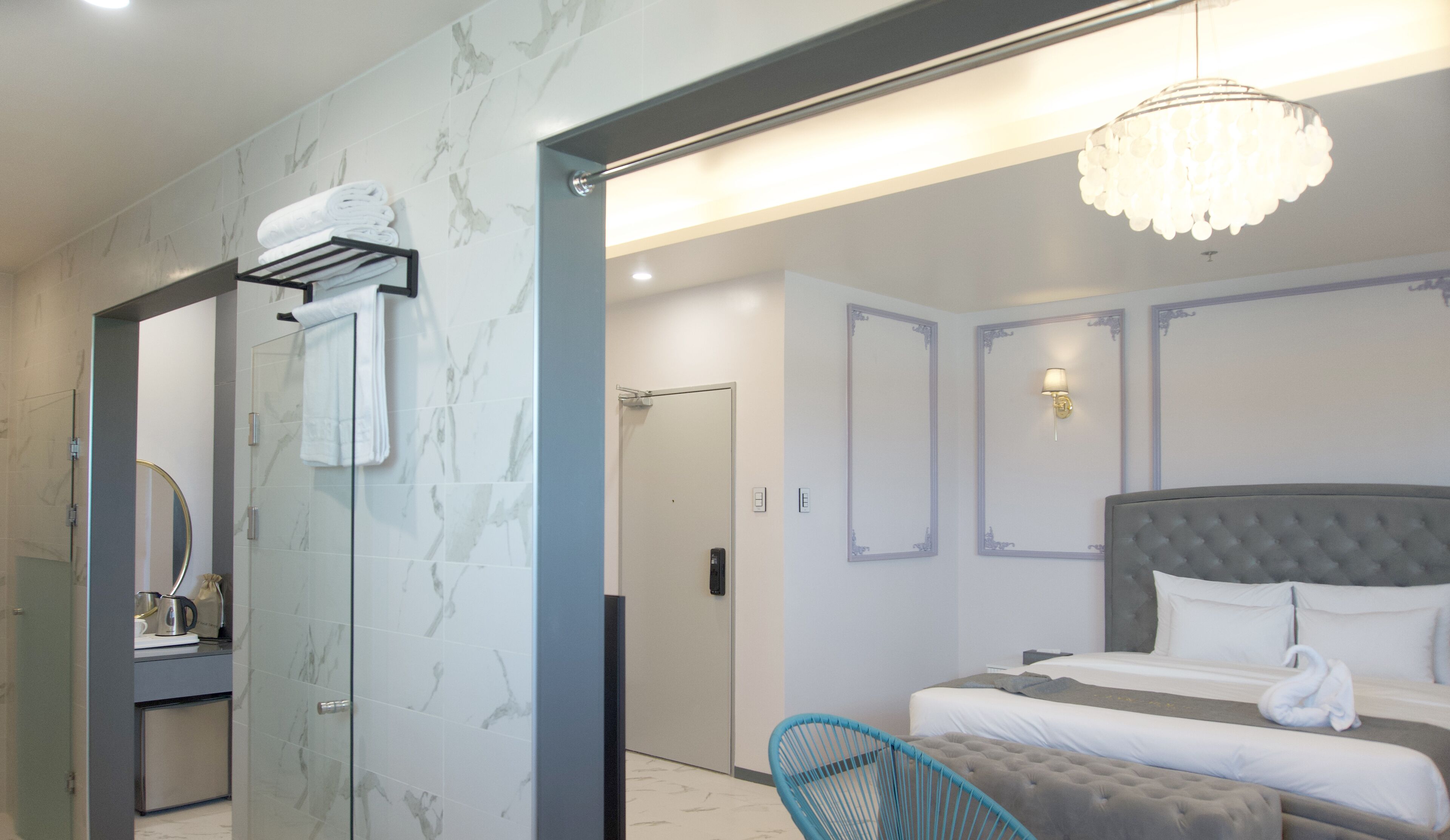 Quarto de hotel moderno com uma cama grande, área de estar, banheiro com chuveiro e um lustre.
