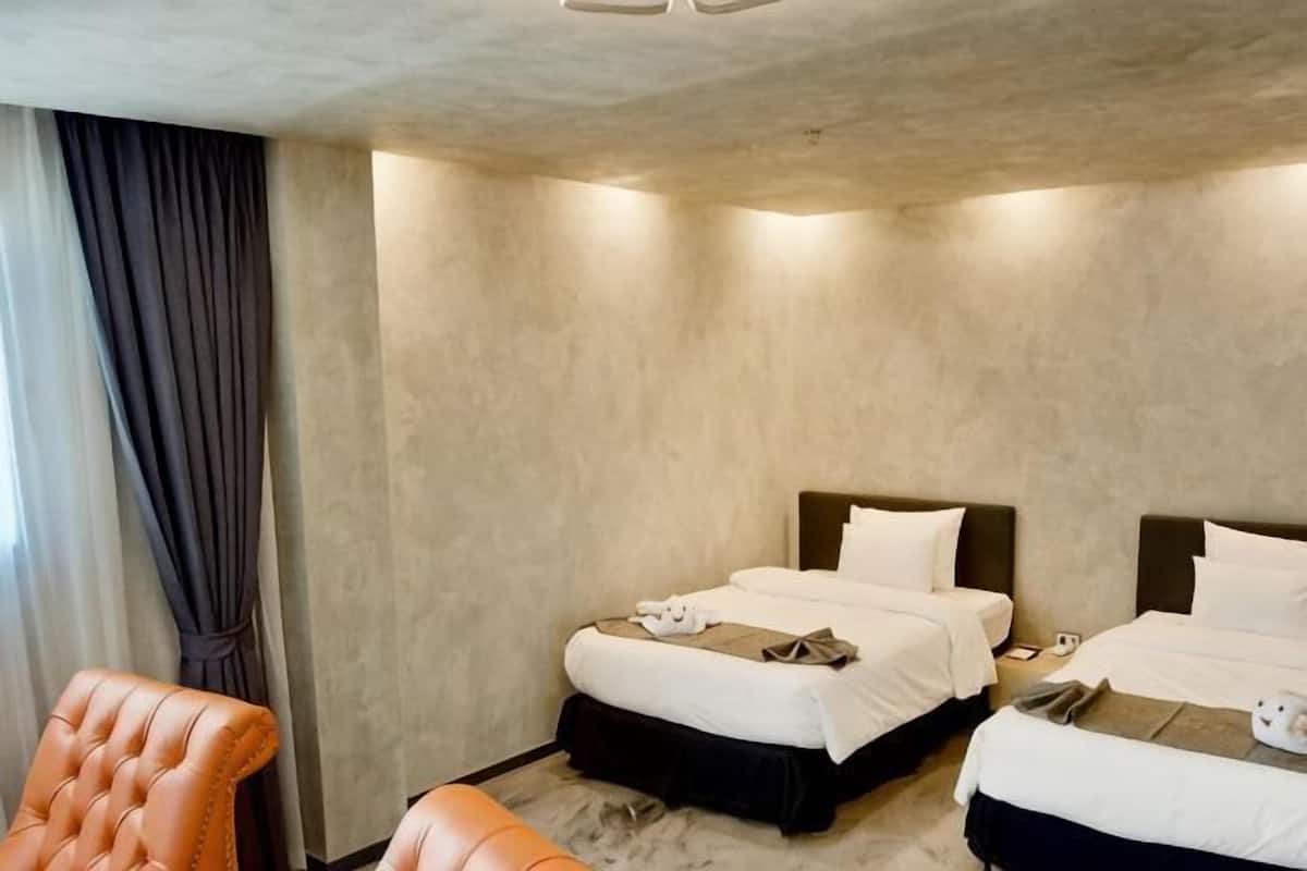 A hotel room with two beds, a sofa, and a large window with curtains.