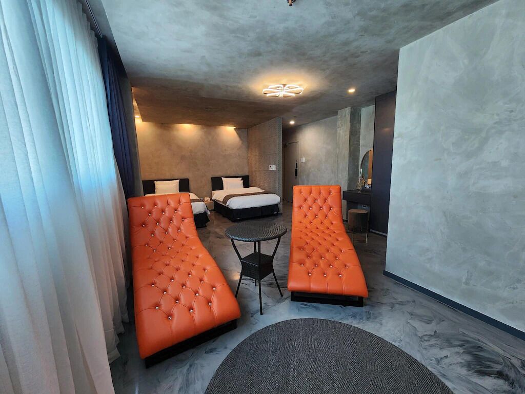 Una habitación de hotel moderna con una cama, dos sofás naranjas, una mesita redonda y un espejo grande.