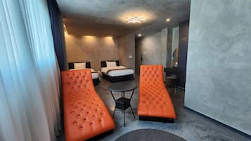 Una habitación de hotel moderna con una cama, dos sofás naranjas, una mesita redonda y un espejo grande.