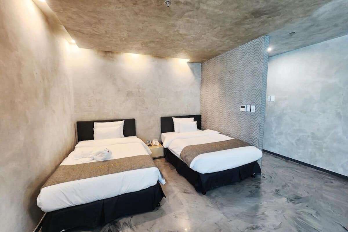 A modern hotel room with two beds, a marble floor, and a textured wall.