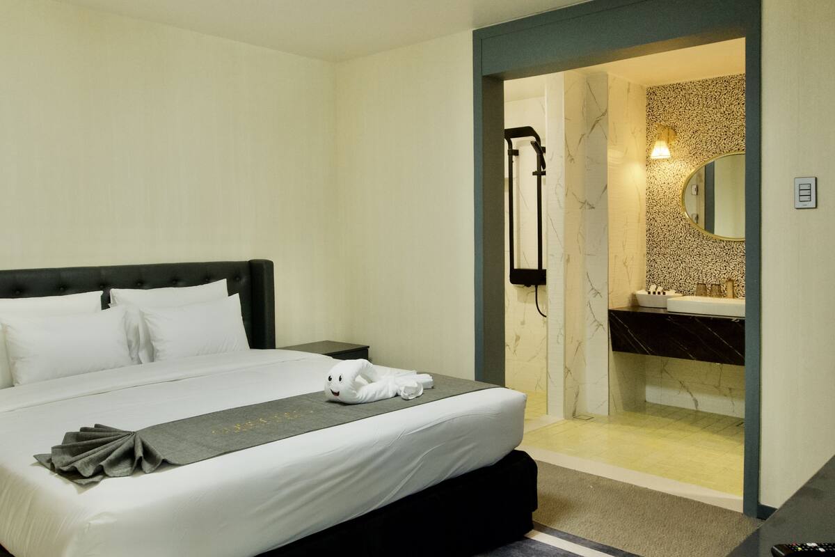 A hotel room with a bed, a bathroom with a mirror, and a towel on the bed.