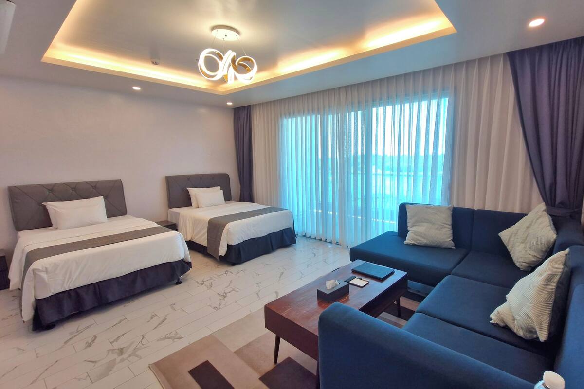 A hotel room with two beds, a sofa, a coffee table, and a large window with curtains.
