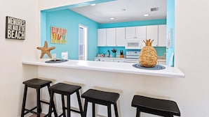 Cocina con una pared de acento color aguamarina, armarios blancos y una isla central con taburetes.