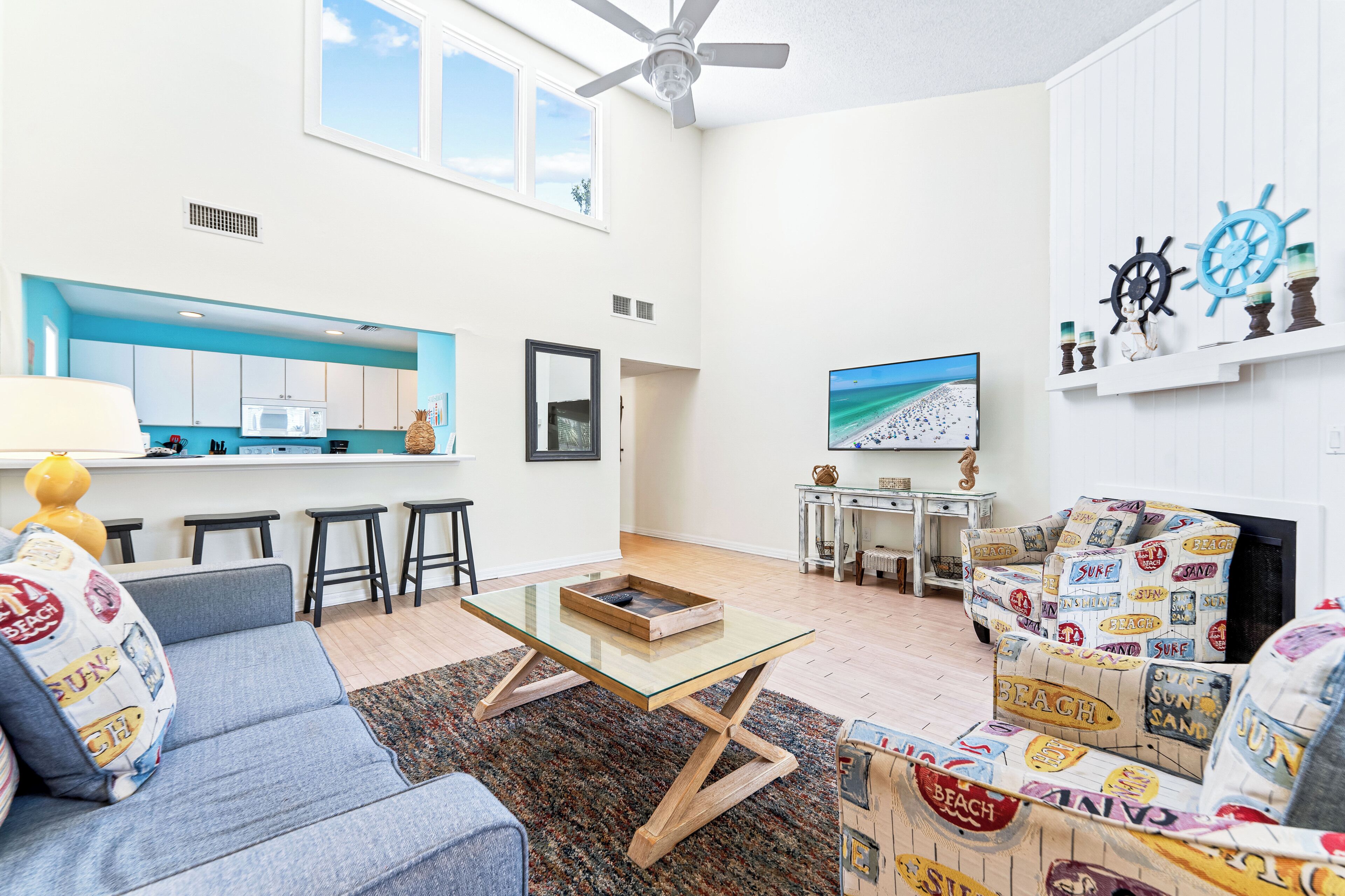A modern living room with a sofa, coffee table, and a TV. There's a kitchen area with a microwave and a window.