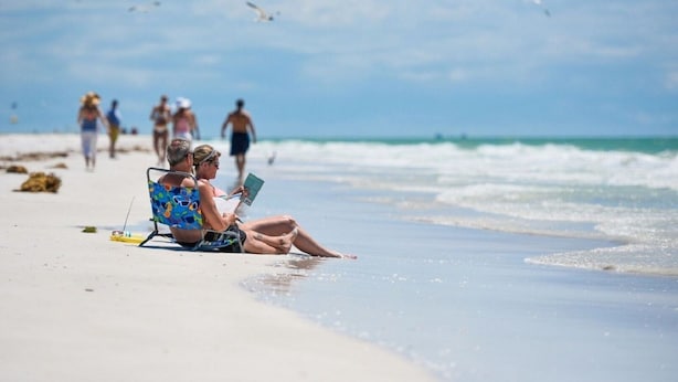 Escena de playa con una pareja sentada en una silla de playa, leyendo un libro.