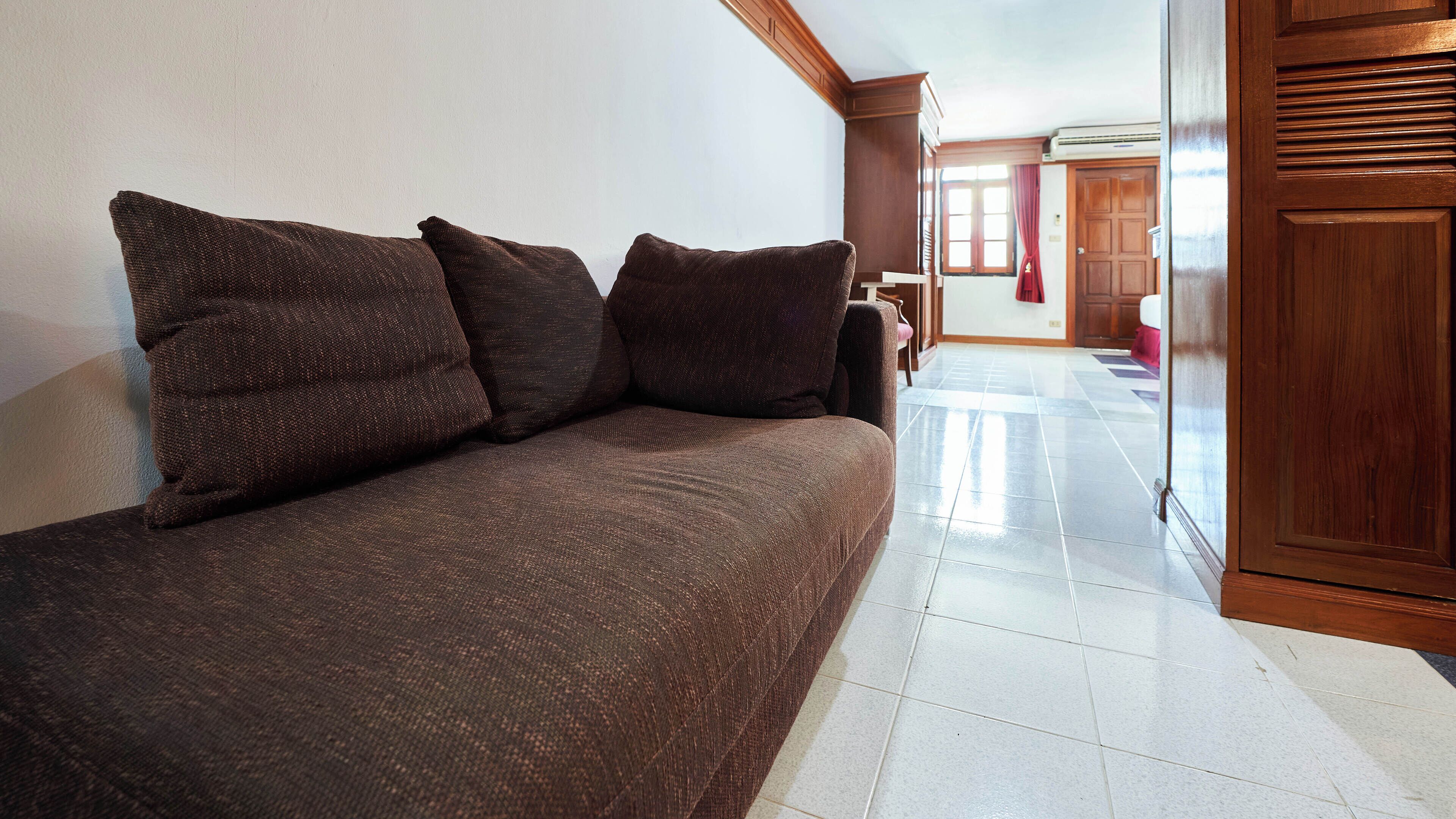 A room with a brown sofa, a wooden wardrobe, and a tiled floor.