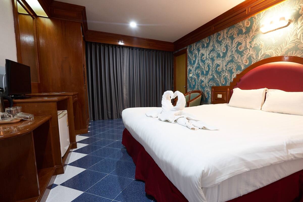 Una habitación de hotel con una cama grande, cabecera de madera, un televisor sobre un escritorio y un mostrador de recepción.