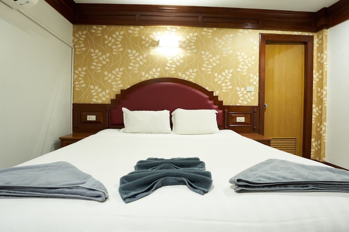 Una cama bien hecha con dos almohadas, un cabecero de madera y una pared con estampado floral.