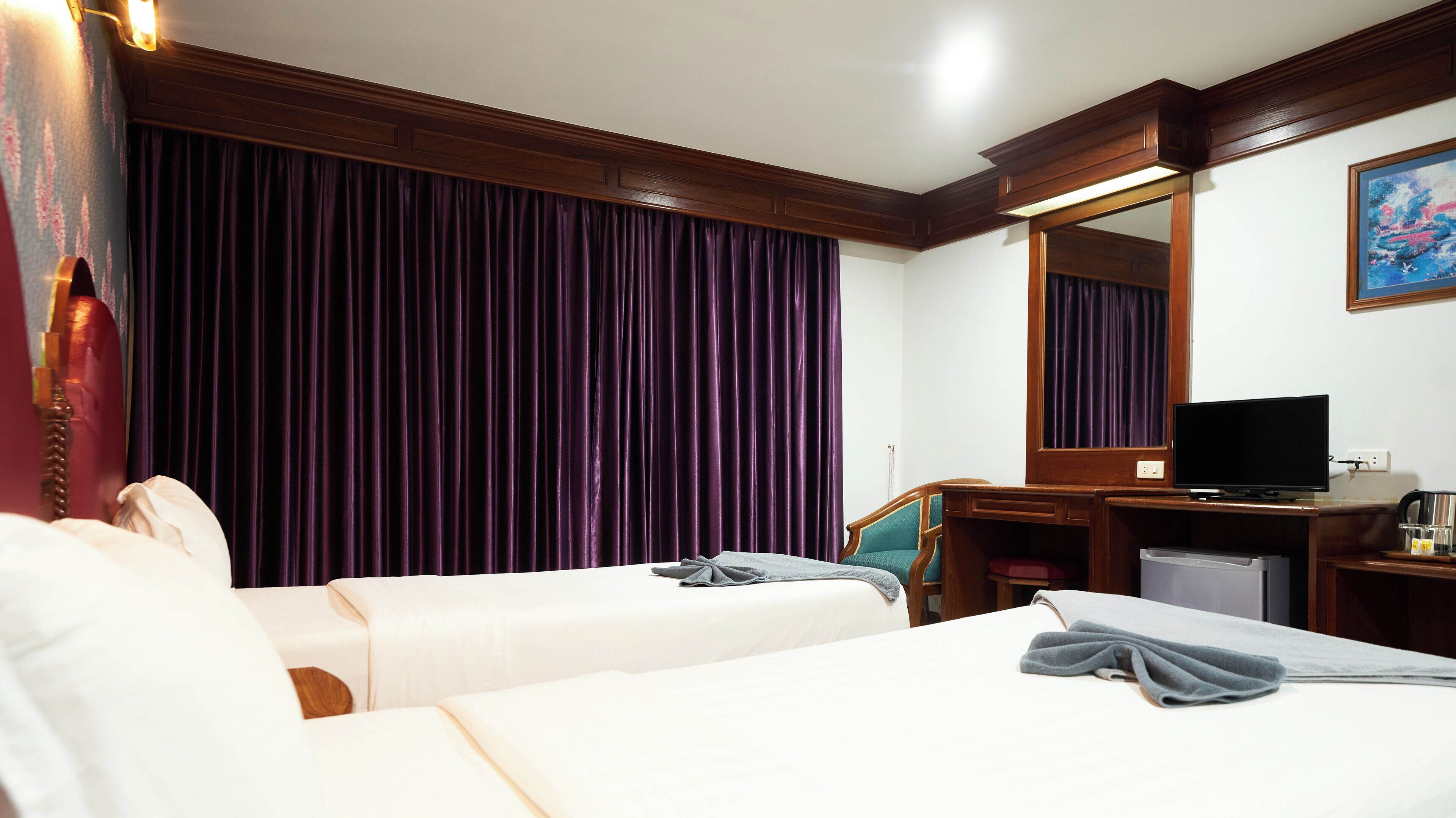 Une chambre d’hôtel avec deux lits, un bureau avec une télévision, une machine à café et une grande fenêtre avec des rideaux violets.