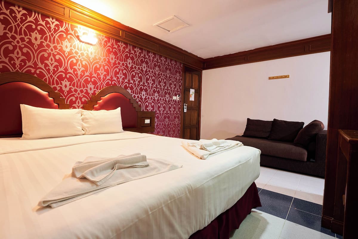 Habitación de hotel con una cama grande, cabecera de madera, sofá marrón y papel tapiz estampado.