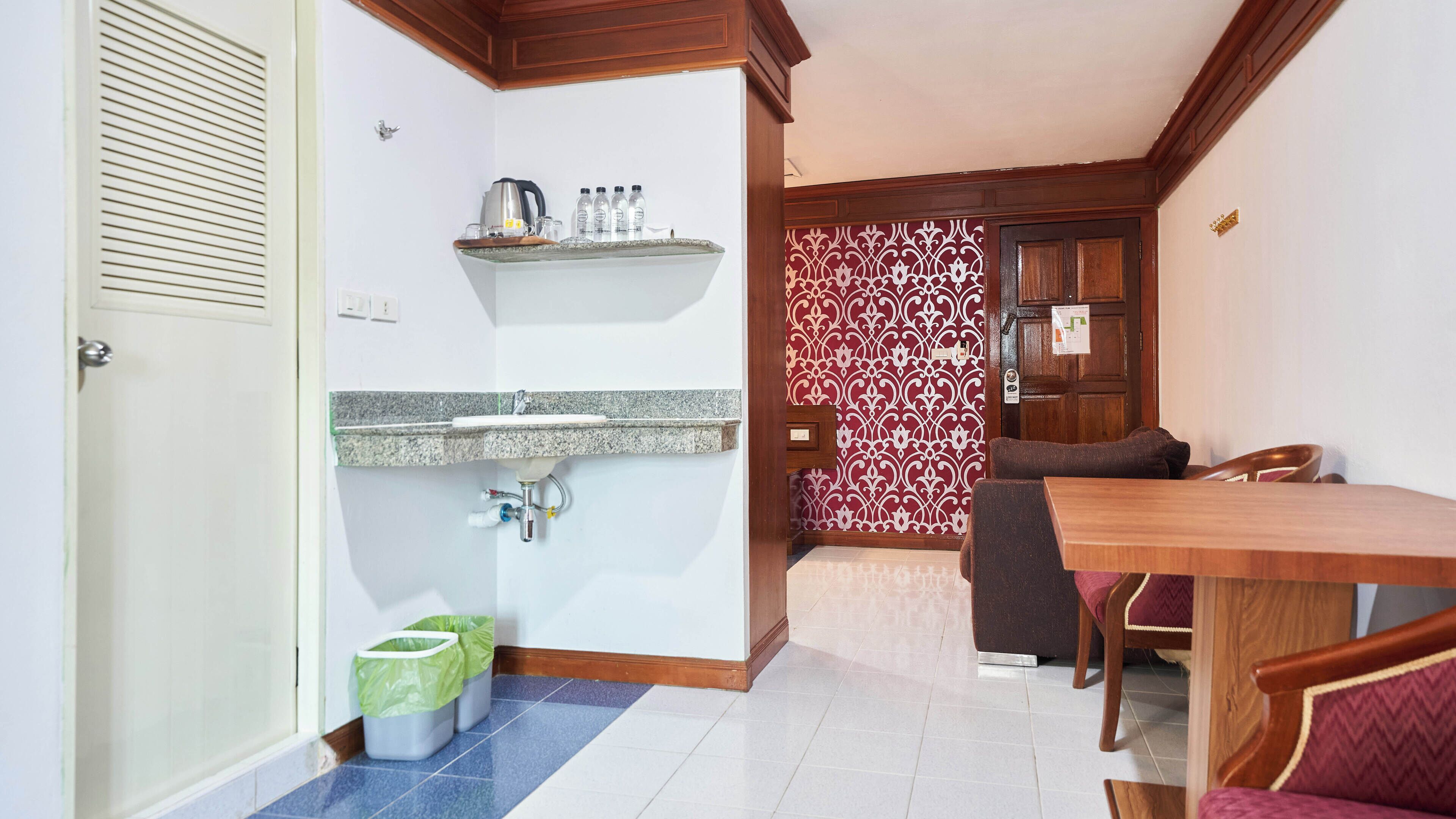 A compact kitchen with a granite countertop, a sink, and a coffee maker. There are two trash bins and a dining area with a wooden table and chairs.