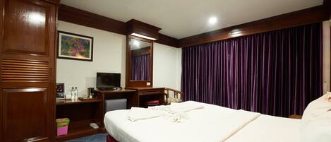 A hotel room with a bed, a desk with a television, a dresser, and a large window with purple curtains.