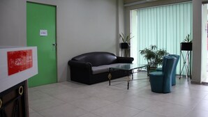 A room with a closed door, a black leather sofa, a glass coffee table, and two blue chairs. - Sandakan Inn (Sandakan)