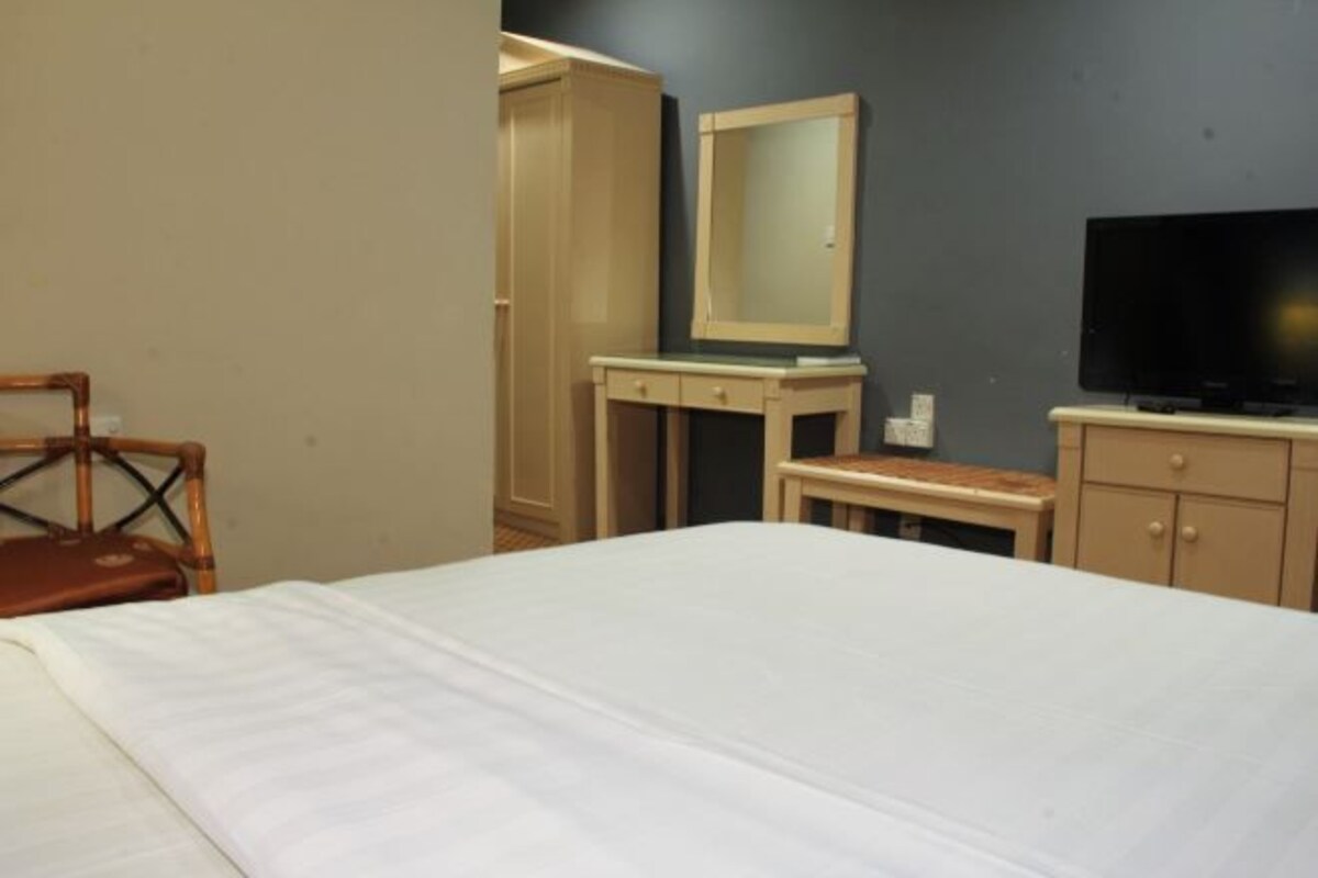 A hotel room with a bed, a television, a desk with a mirror, and a wardrobe.