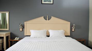 A neatly made bed with a wooden headboard, two bedside tables with clocks, and a framed picture on the wall.