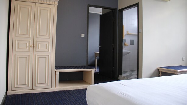 A hotel room with a bed, a wardrobe, a bench, a sink, and an air conditioning unit. - Sandakan Inn (Sandakan)