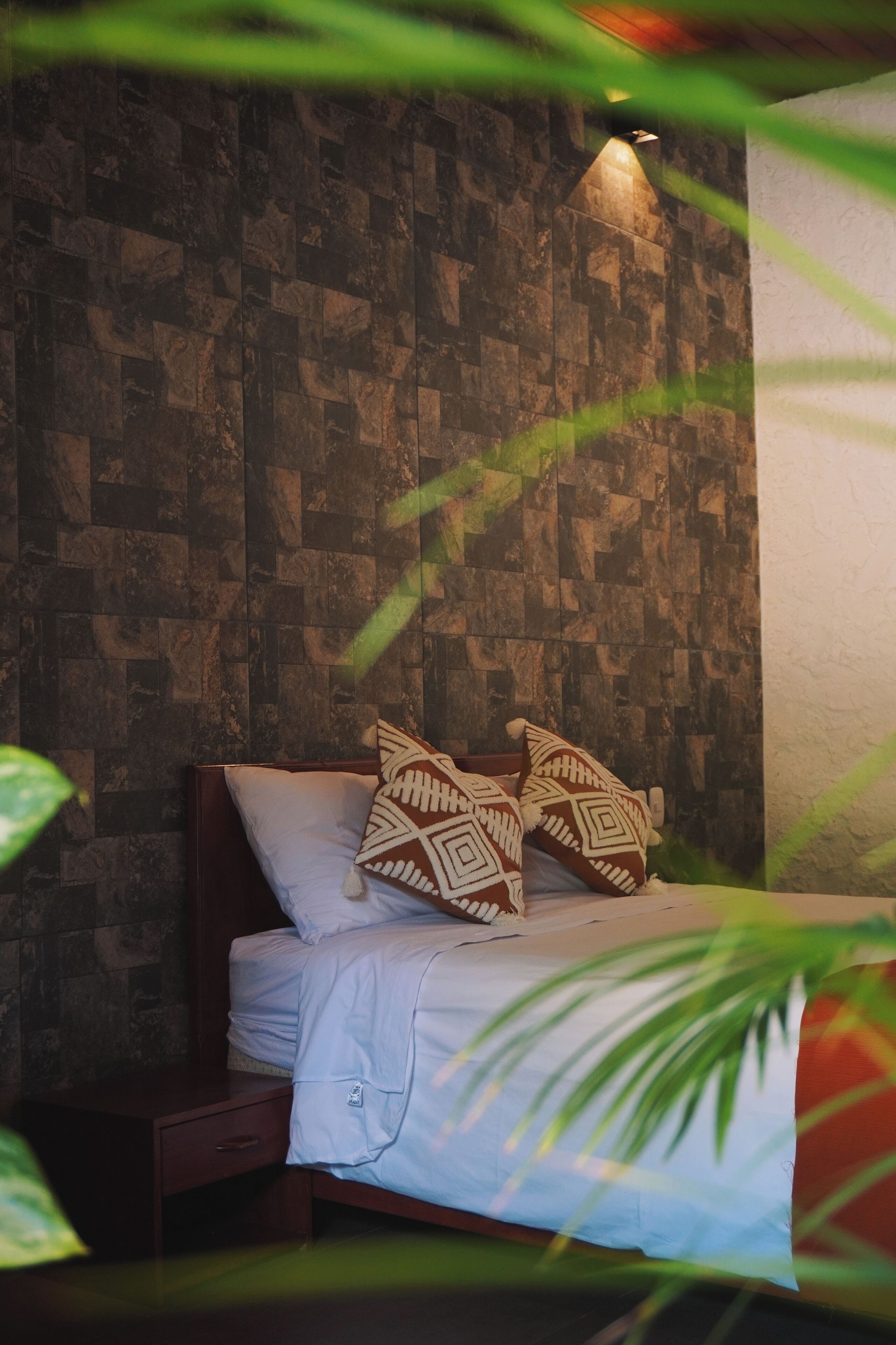 Un dormitorio con cama, almohadas, una mesita de noche y una pared con diseño de piedra.